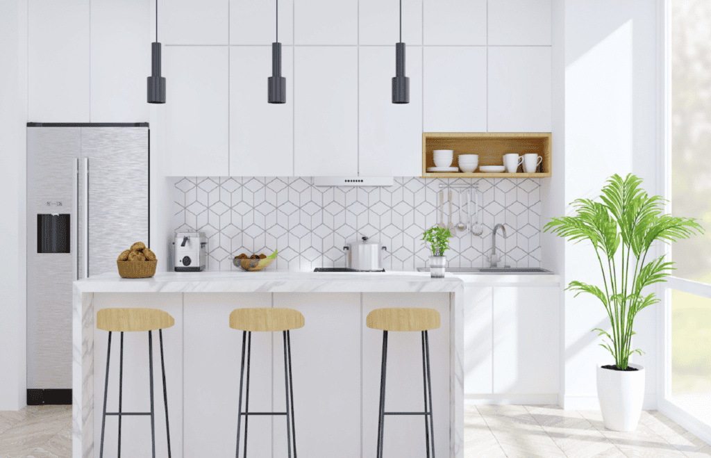 A modern kitchen with white cabinets, a geometric tile backsplash, and a marble island with three wooden stools. Pendant lights hang over the island, and a potted plant is in the corner. Appliances, a fruit bowl, and various kitchen items are displayed on the countertop—perfect for those considering Kitchen Remodeling Orlando Florida.