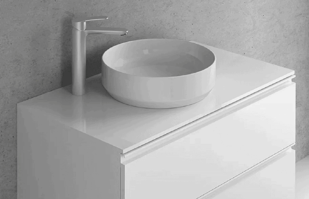 A modern bathroom vanity with a sleek design. It features a white, round vessel sink on top of a glossy white cabinet with two drawers. A tall, silver faucet is mounted to the left of the sink against a light gray wall—a perfect choice for Bathroom Remodeling Orlando Florida.