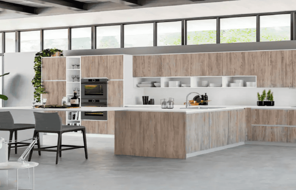 A modern kitchen with natural wood cabinets and white countertops. An island features a sink and bar seating. Built-in appliances are visible on the left. Open shelves display dishes and plants. There's a dining table with gray chairs in the foreground, perfect for those considering kitchen remodeling in Orlando Florida.