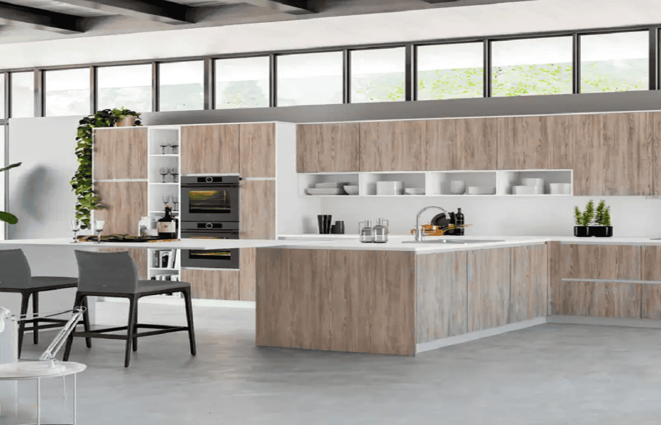 A modern kitchen with natural wood cabinets and white countertops. An island features a sink and bar seating. Built-in appliances are visible on the left. Open shelves display dishes and plants. There's a dining table with gray chairs in the foreground, perfect for those considering kitchen remodeling in Orlando Florida.