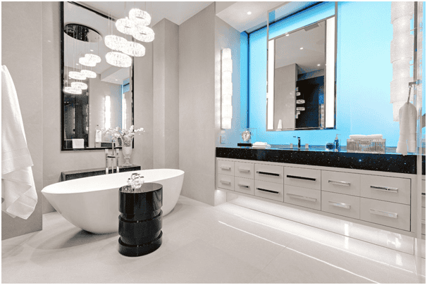 A modern bathroom with a freestanding oval bathtub, a small black table, and a white towel. The vanity area showcases bathroom countertops from Orlando, Florida, featuring a long black surface with double sinks and multiple drawers. Bright lights illuminate the space while large mirrors reflect the sleek decor.